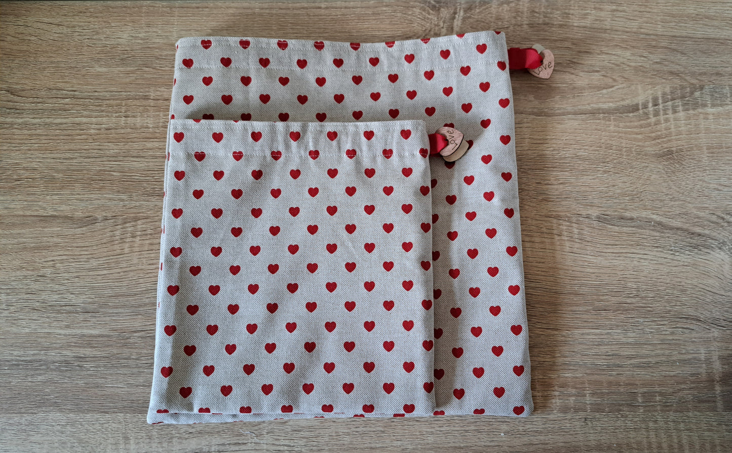 Two fabric gift bags with red heart patterns on a wooden surface