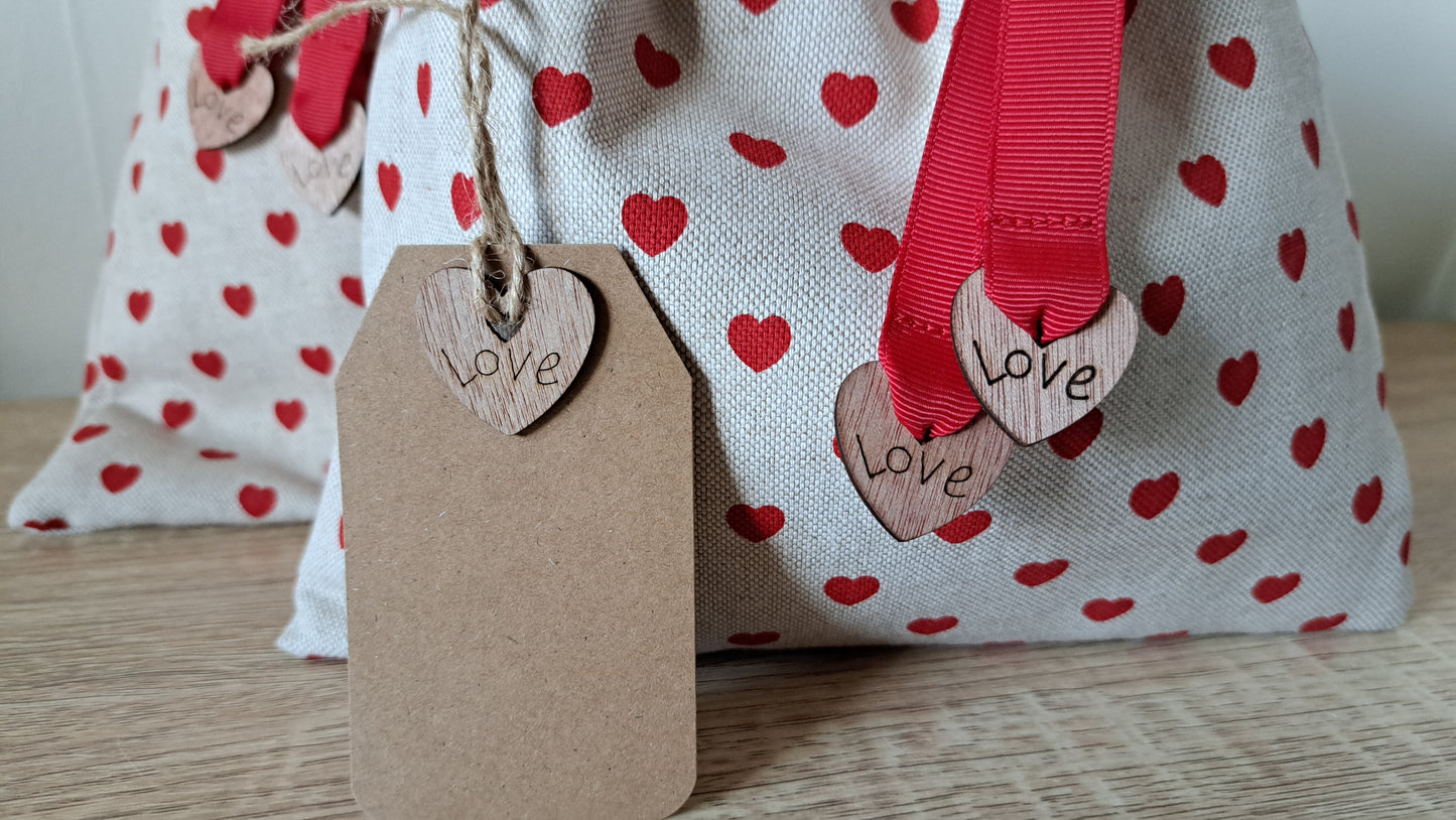 Fabric bag with red heart patterns, a brown 'Love' tag, and red ribbons.