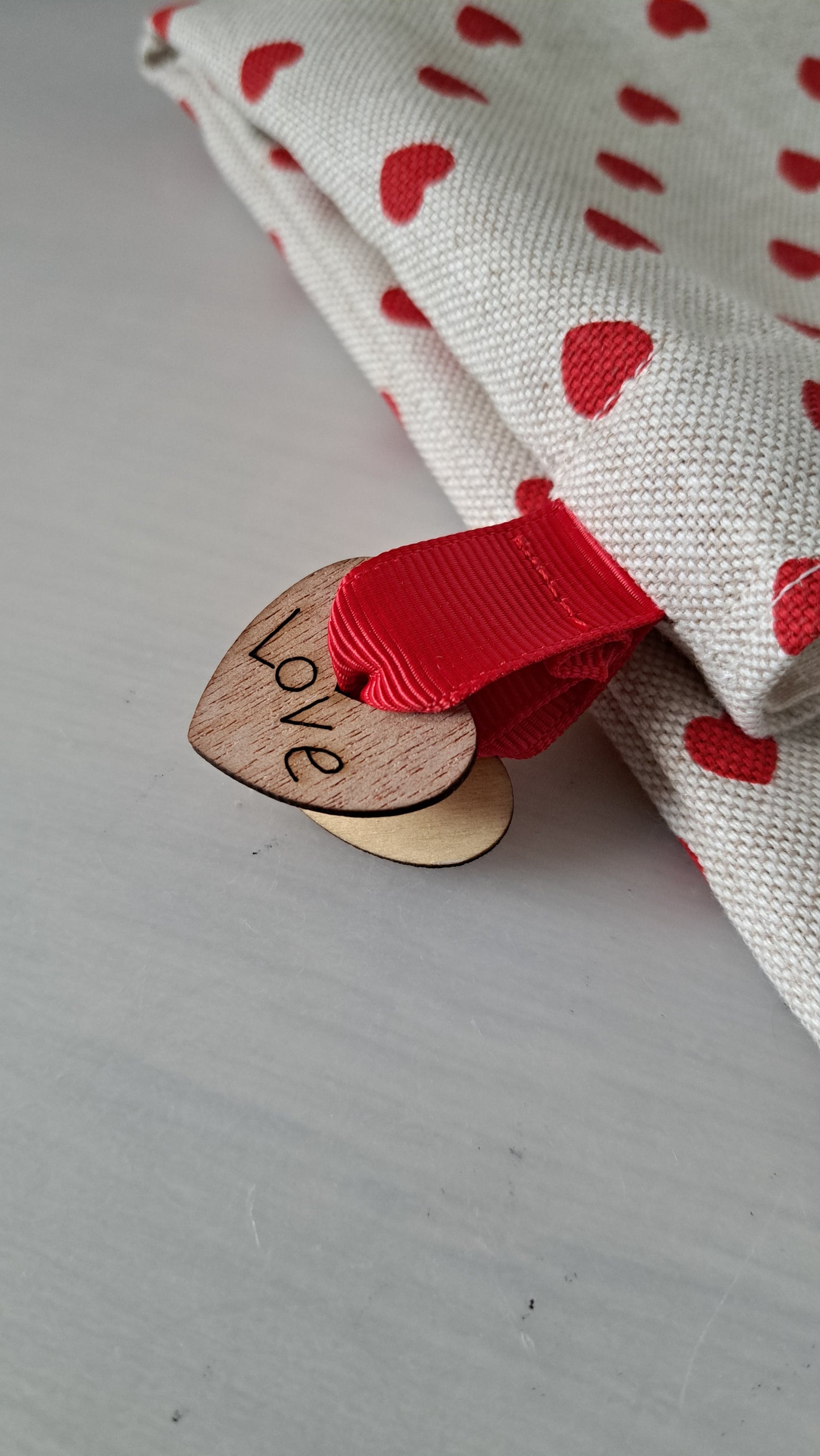 Heart-shaped wooden tag with 'love' on a fabric background with red heart patterns.