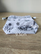 White drawstring bag with black floral and star pattern on a wooden surface, with measurements indicated.