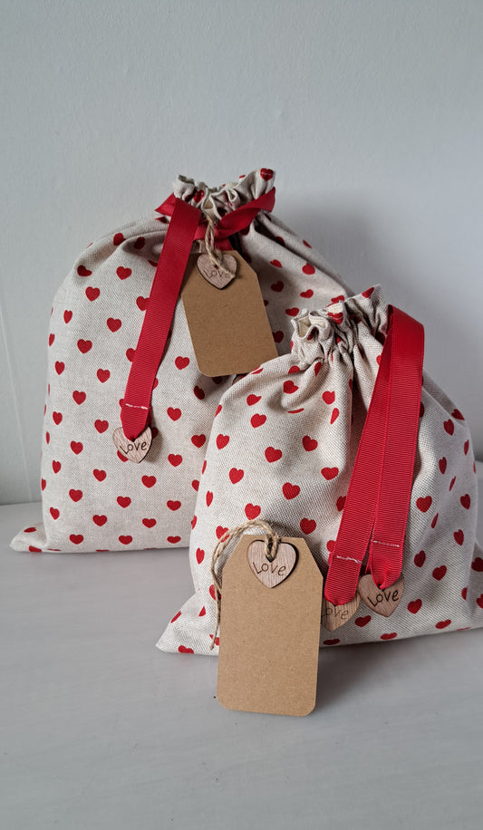 Two fabric bags with red heart patterns and red drawstrings on a gray background.